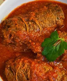 some meat and sauce in a bowl with a leafy green garnish on top