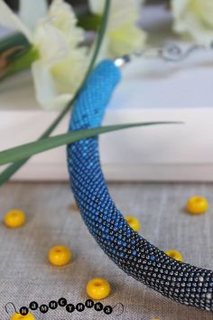 a blue and yellow beaded necklace sitting on top of a table next to flowers