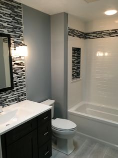 a white toilet sitting under a bathroom mirror next to a sink and bathtub in a bathroom