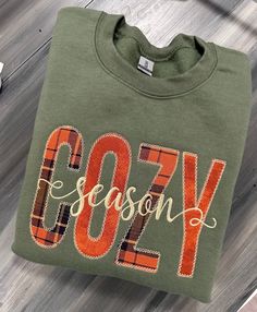 a green sweatshirt with the word cozy on it sitting on top of a wooden floor