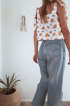 a woman standing in front of a wall wearing blue jeans and a top with oranges on it