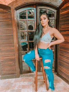 a woman standing on top of a wooden chair in front of a door wearing ripped jeans