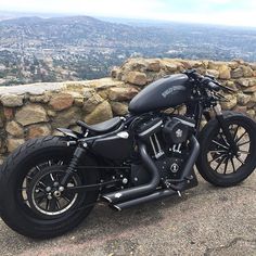 a black motorcycle parked next to a stone wall on top of a hill in front of a city