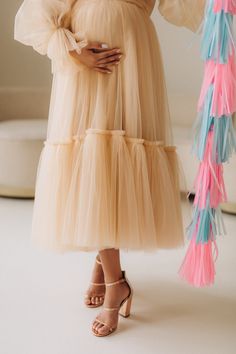 a pregnant woman in a beige dress holding a pink and blue tasseled fan