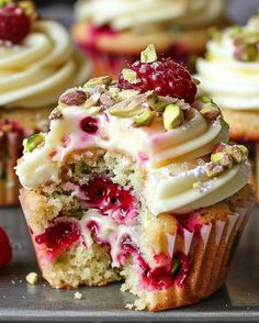 cupcakes with white frosting, raspberries and pistachio on top