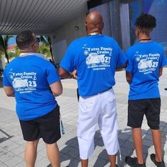 three men in blue shirts are standing on the sidewalk with their backs turned to the camera