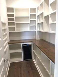 an empty room with white shelving and wood flooring in the center is a wine cellar built into the wall