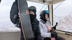 two people sitting in a ski lift with snowboards on their shoulders and helmets on