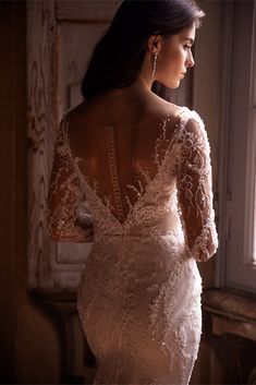 a woman in a wedding dress looking out the window with her back to the camera