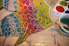 a colorful fish is being painted with watercolors and paintbrushes on the table