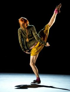 a woman with red hair is doing a dance move on the floor in front of a black background