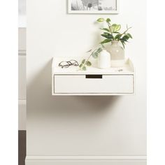 a small white table with a plant and sunglasses on it next to a framed photo