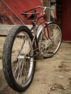 a bicycle parked in front of a red barn with an old fashioned bike leaning against it