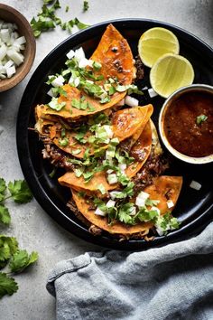 a black plate topped with nachos next to a bowl of salsa and cilantro