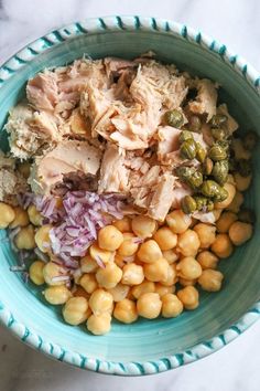 a bowl filled with chickpeas, peas and chicken salad on top of a marble counter