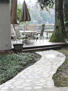 a stone path leading to a patio with an umbrella and table in the back ground