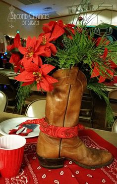 a cowboy boot with red flowers in it sitting on a table next to a cup