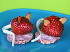 two small stuffed animals made to look like strawberries on a blue plate with green background