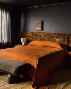 a bed with an orange bedspread in a dark room next to a window