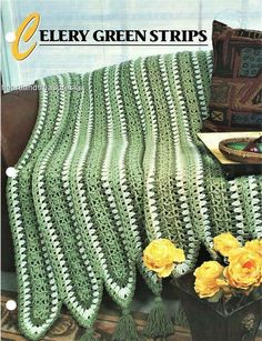 a green crocheted afghan sitting on top of a couch next to yellow flowers