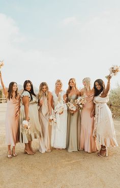 a group of women standing next to each other in front of a dirt field holding bouquets