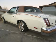 a white car parked in front of a house next to a brown and tan car