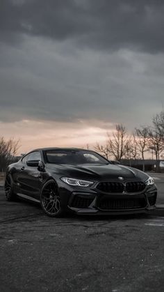 a black car parked in a parking lot with dark clouds above it and the sun setting