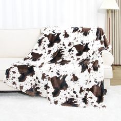 a cow print blanket sitting on top of a couch next to a white chair and lamp