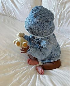 a baby sitting on top of a bed holding a teddy bear