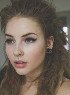 a young woman with blue eyes and piercings on her nose is looking at the camera