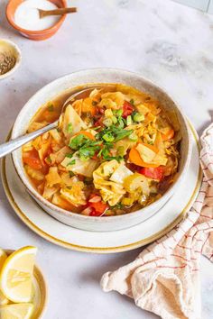 a white bowl filled with vegetable soup on top of a table next to sliced lemons