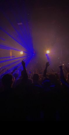 a crowd at a concert with their hands up in the air and lights shining down on them