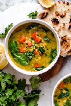 two bowls filled with soup next to sliced lemons and pita bread