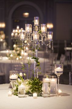 a table with candles and flowers on it in front of a chandelier filled with glass vases