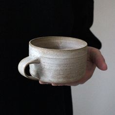 a person holding a coffee cup in their hand with the handle extended to hold it