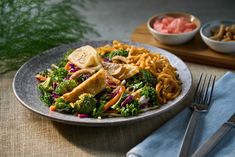 a plate with noodles, broccoli and meat on it next to silverware