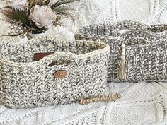 two knitted baskets sitting on top of a bed next to a vase with flowers