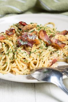 pasta with bacon and parmesan cheese on a plate next to a silver fork