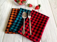 a bowl of strawberries sits next to two plaid napkins and a silver spoon