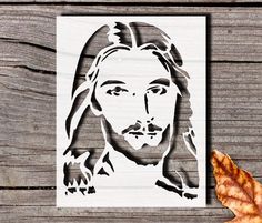 a paper cutout of the face of jesus on a wooden surface with leaves around it