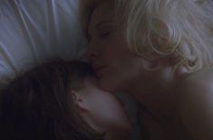 a woman laying in bed with her face close to another woman's chest and head