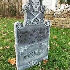 a tombstone with a skull and cross on it in the grass next to a house