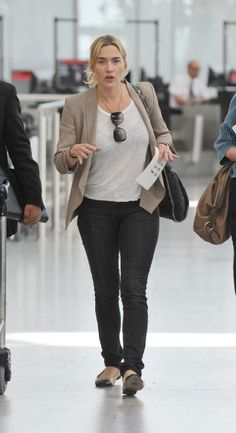 a woman is walking through an airport with her hand in her pocket and luggage behind her