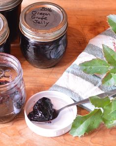 three jars filled with jam sitting on top of a wooden table next to green leaves