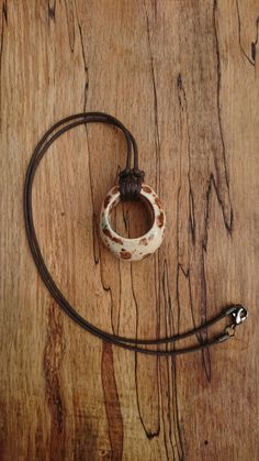 a brown and white bracelet sitting on top of a wooden table next to a leather cord