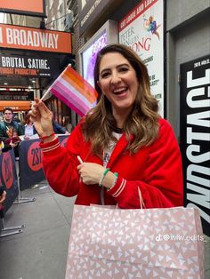 a woman in a red jacket is holding a shopping bag and smiling at the camera