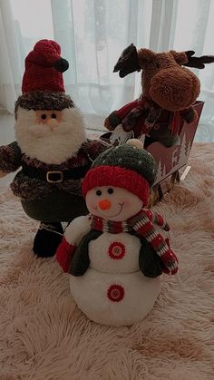 two stuffed animals are sitting next to a snowman on the floor in front of a window