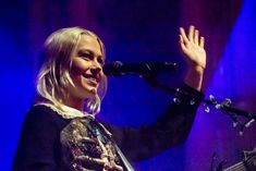 a woman with blonde hair is singing into a microphone and holding her hand up in the air