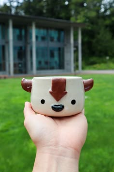 a hand holding a small ceramic animal cup in front of a building