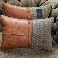 two brown leather pillows sitting on top of a gray couch next to a black tag